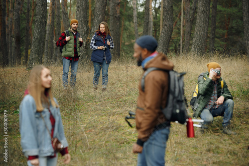 Group of friends on a camping or hiking trip in autumn day. Men and women with touristic backpacks going throught the forest, talking, laughting. Leisure activity, friendship, weekend.
