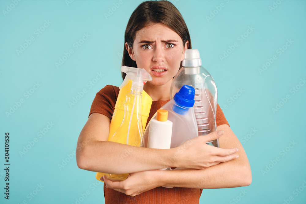 Shocked girl holding empty plastic detergents in hands while scaredly looking in camera over colorful background Shocked girl holding empty plastic detergents in hands while scaredly looking in camera over colorful background