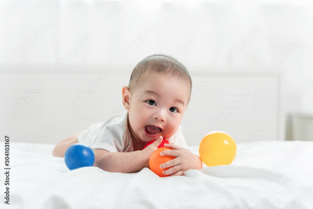 Asian baby is laughing and playing toy ball on white bed with feeling happy and cheerful and the baby that crawling on the bed.Baby family concept Asian baby is laughing and playing toy ball on white bed with feeling happy and cheerful and the baby that crawling on the bed.Baby family concept