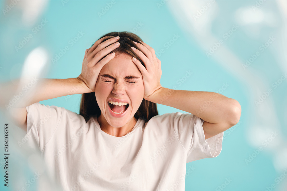 Irritated girl closing eyes while angrily screaming on plastic over colorful background Irritated girl closing eyes while angrily screaming on plastic over colorful background