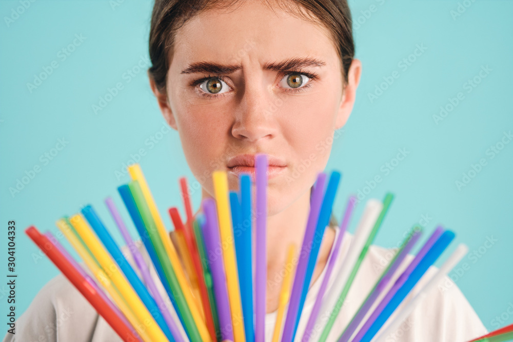 Close up girl with colorful straws sadly looking in camera over colorful background. Stop using plastic straws Close up girl with colorful straws sadly looking in camera over colorful background. Stop using plastic straws