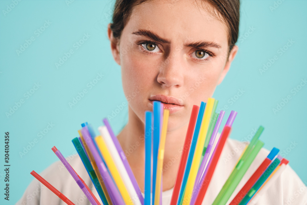Close up unhappy girl with plastic straws tiredly looking in camera over colorful background. Stop using plastic straws Close up unhappy girl with plastic straws tiredly looking in camera over colorful background. Stop using plastic straws