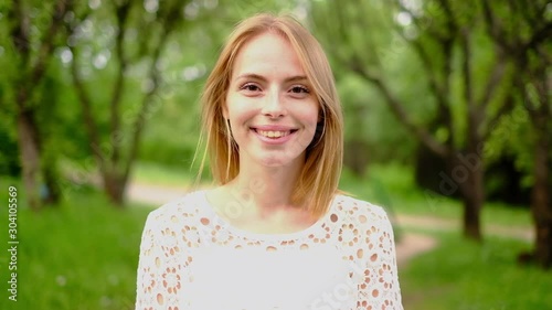 Beautiful attractive young woman posing in spring park wearing white knitted top and blue jeans,, slow motion photo