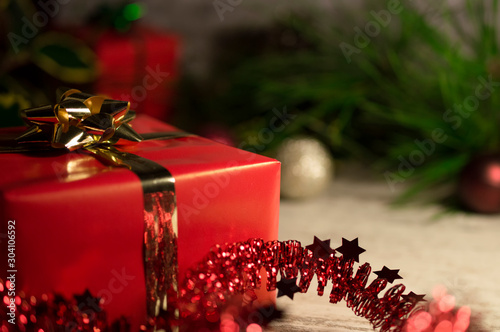 Christmas gift - box of red color in the foreground. Still life with a distinctive box - a Christmas present in the foreground. Photo with bokeh, focus focused on gift.
