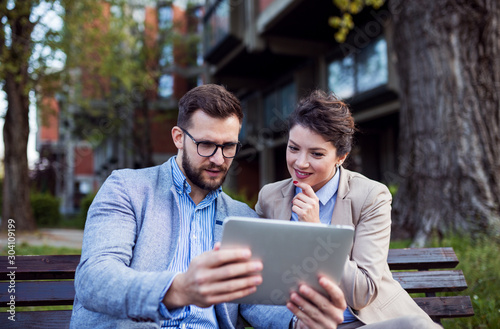 Business couple using digital tablet on park bench
