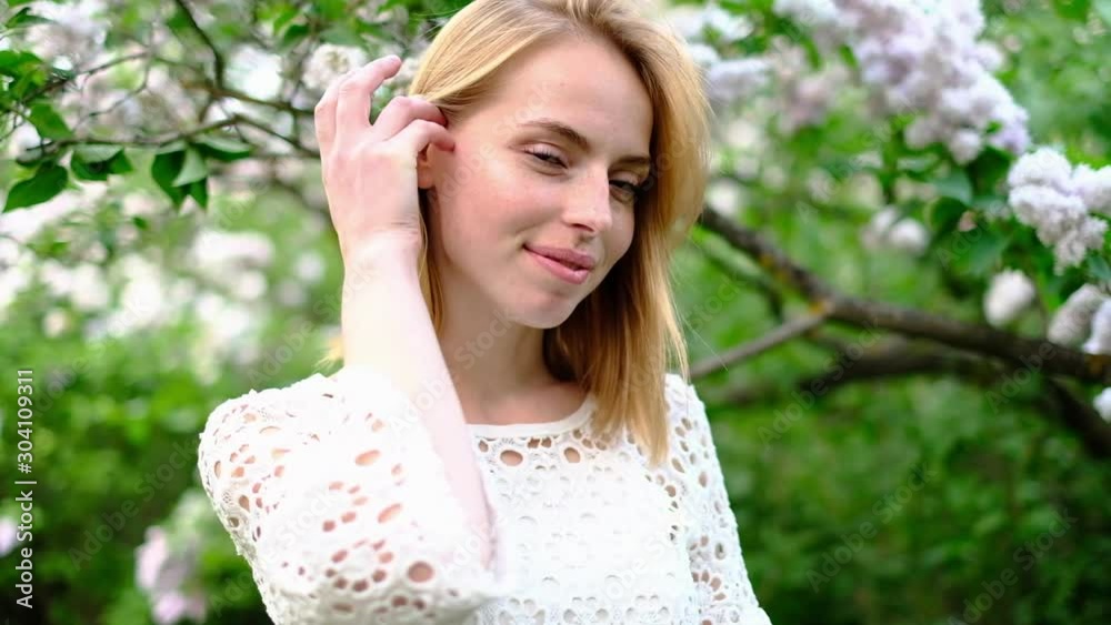 Beautiful attractive young woman posing in spring park wearing white knitted top and blue jeans,, slow motion Beautiful attractive young woman posing in spring park wearing white knitted top and blue jeans,, slow motion