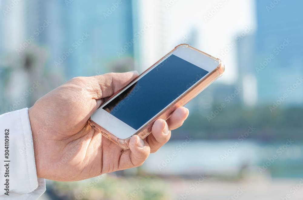 close up handsome man using hand typing smartphones and touch screen working search with app devices outdoor in city with sunrise and building background. 5G technology connecting the world.