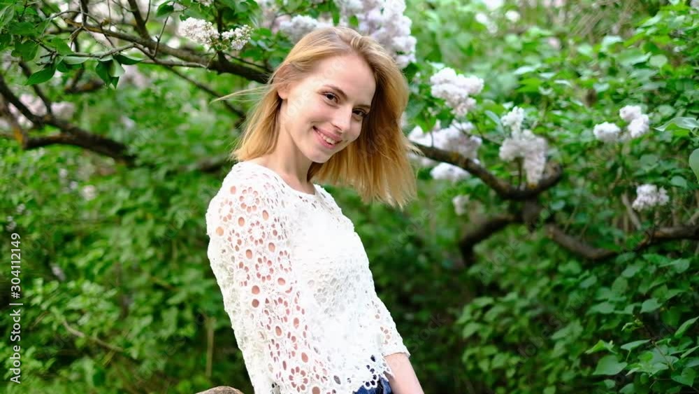 Beautiful attractive young woman posing in spring park wearing white knitted top and blue jeans,, slow motion Beautiful attractive young woman posing in spring park wearing white knitted top and blue jeans,, slow motion