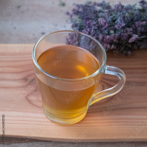 Warm oregano tea in a glass cup on wooden board