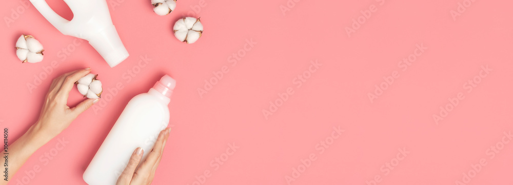 Eco cleaning concept. Women's hands hold white plastic packaging of laundry detergent, liquid powder, washing conditioner, cotton flowers on pink background. Flat lay top view. Bio organic product