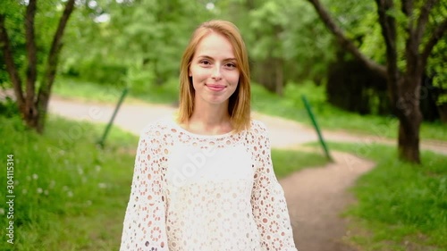 Beautiful attractive young woman posing in spring park wearing white knitted top and blue jeans,, slow motion photo