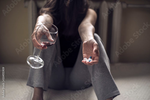 a young girl sitting in a dirty room, with a glass of wine, and holds pills in her hand. Poisoning when mixing alcohol and drugs. Polydrug addiction in women