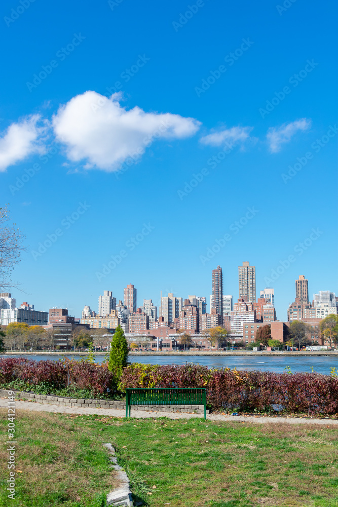 Shoreline of Astoria Queens New York with a Bench looking towards the East River and the Manhattan and Roosevelt Island Skyline in the background Shoreline of Astoria Queens New York with a Bench looking towards the East River and the Manhattan and Roosevelt Island Skyline in the background