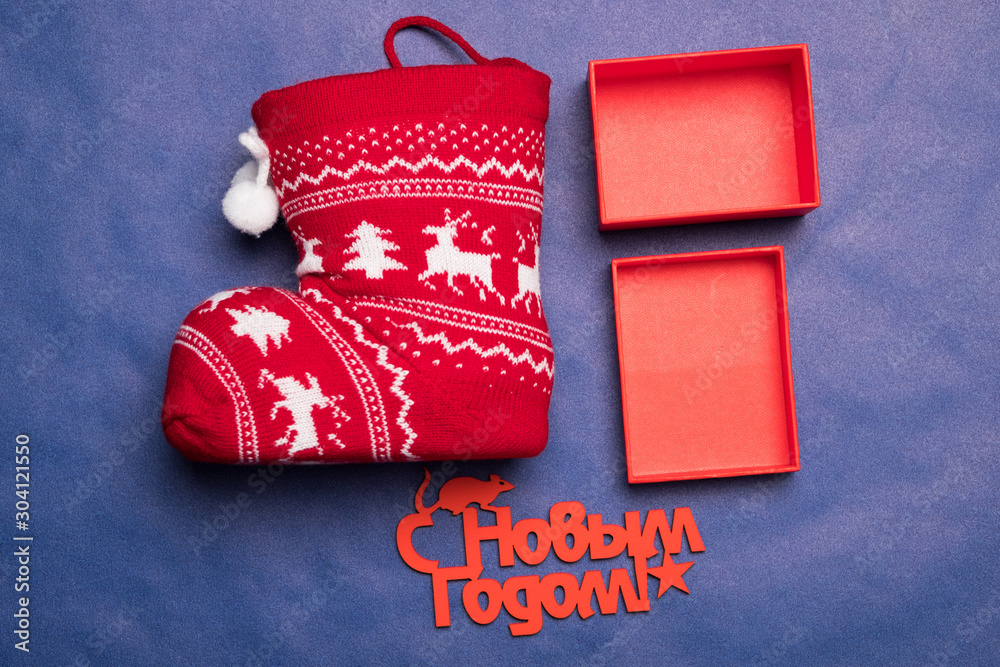 Naklejka premium Christmas background with the inscription in Russian New Year's studio image. Red gift box with christmas sock on a blue background. Greeting Christmas card.