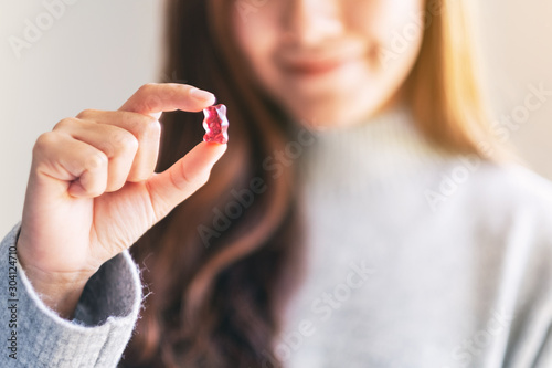Closeup image of a beautiful woman holding and looking at a red gummy bear photo