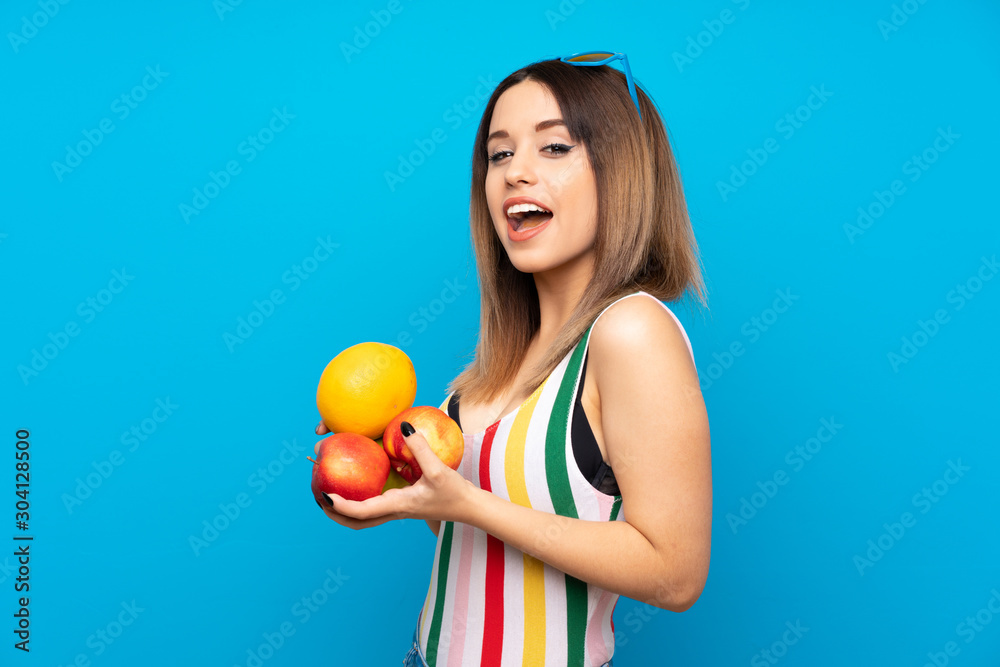 Young woman in summer holidays over blue background holding fruits Young woman in summer holidays over blue background holding fruits
