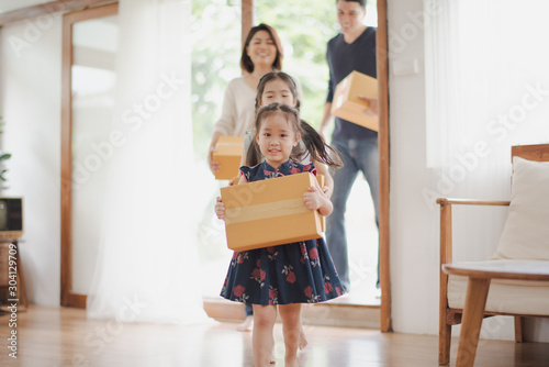 Young Asian family with daughter holds carton and walking in to a new home in moving relocation day which Excited smiling and felling happy. Mother Father and daughter move on a new home concept. photo