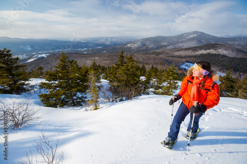 A woman takes in the dramatic vews of the Presidential Range and surrounding hills of the Mount Washington Valley while snowshoeing along Black Cap Mountain Trail near the summit of Black Cap Mountain in the Green Hills Preserve near North Conway, New Hampshire. photo