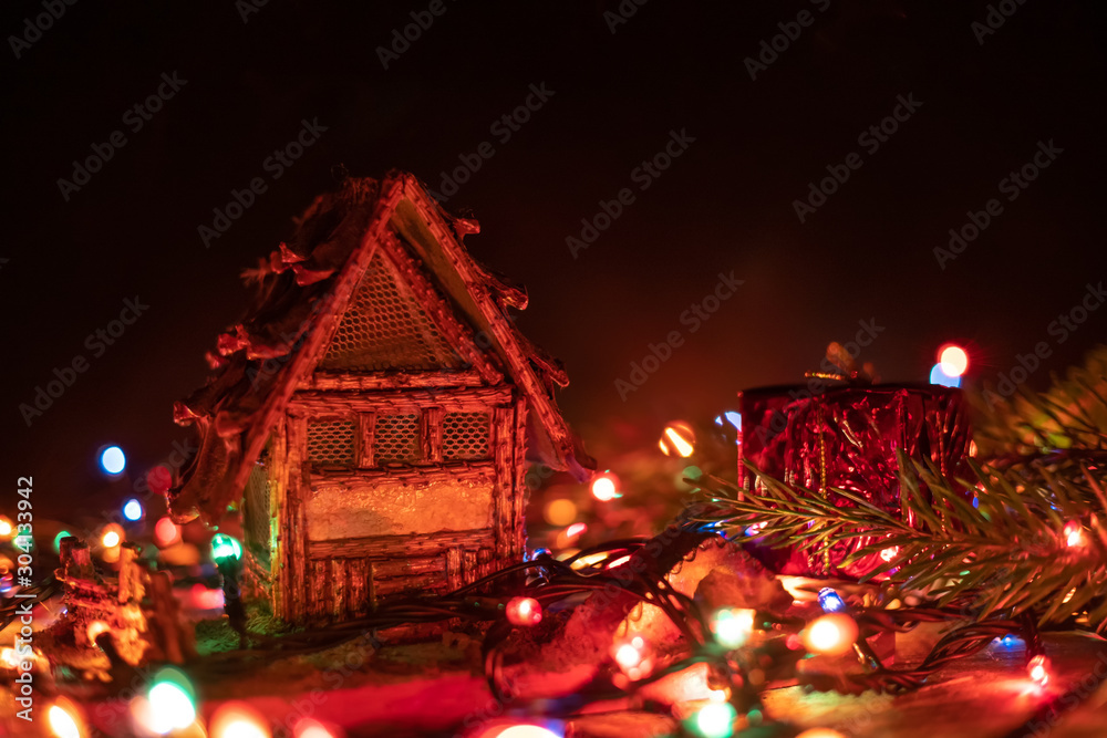 Beautiful, magical Christmas background, greeting card. Small house stands on a wooden background among Christmas lights close-up, in the background a black background with a copy space