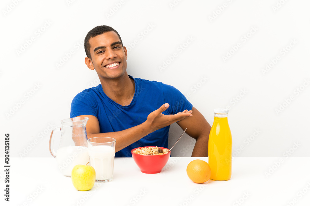 Young man having breakfast in a table extending hands to the side for inviting to come Young man having breakfast in a table extending hands to the side for inviting to come