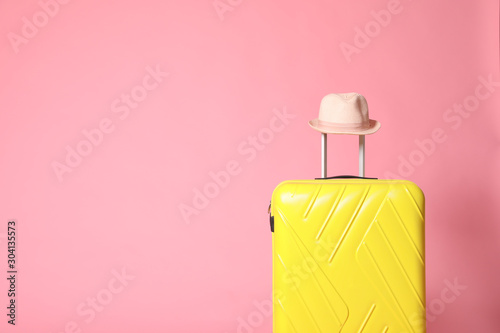 Yellow suitcase with hat on pink background. Space for text
