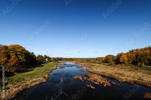 Beautiful daylight view of river Venta in Latvia. Clear sky with orange colored trees in sides. Photo taken in autumn, October.