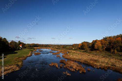 Beautiful daylight view of river Venta in Latvia. Clear sky with orange colored trees in sides. Photo taken in autumn  October.