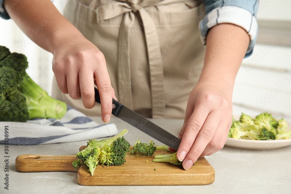 Woman cutting raw broccoli on light grey marble table, closeup Woman cutting raw broccoli on light grey marble table, closeup