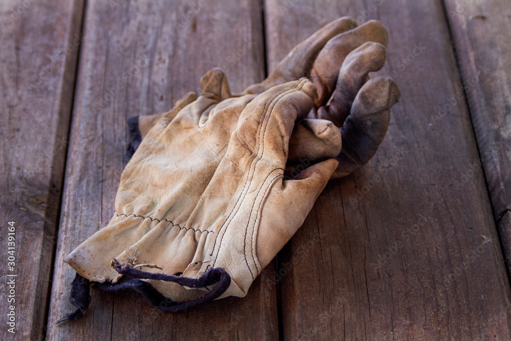 Old worn leather work gloves on wooden background