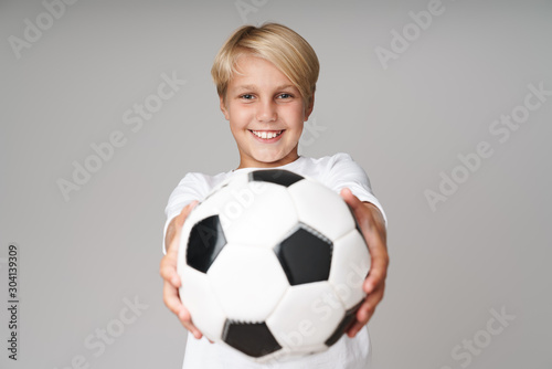 Boy posing isolated over grey wall background holding football. © Drobot Dean