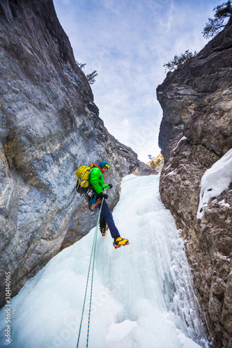 A man  rapells down a icy gully after climbing  Rainbow Serpent (100m WI6) in the Recital Hall, a beautiful rock ampitheatre in the Ghosts in Alberta, Canada. The approach to get to Rainbow Serpent involves climbing numerous moderate pitches of ice that are rapelled down during the descent. photo