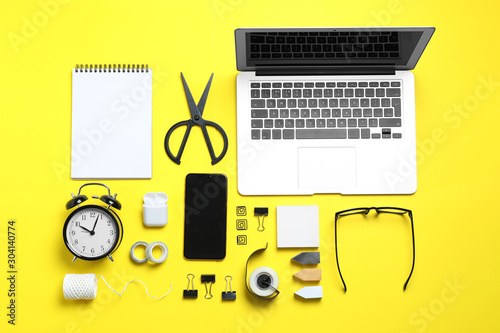 Flat lay composition with laptop, smartphone and stationery on yellow background. Designer's workplace
