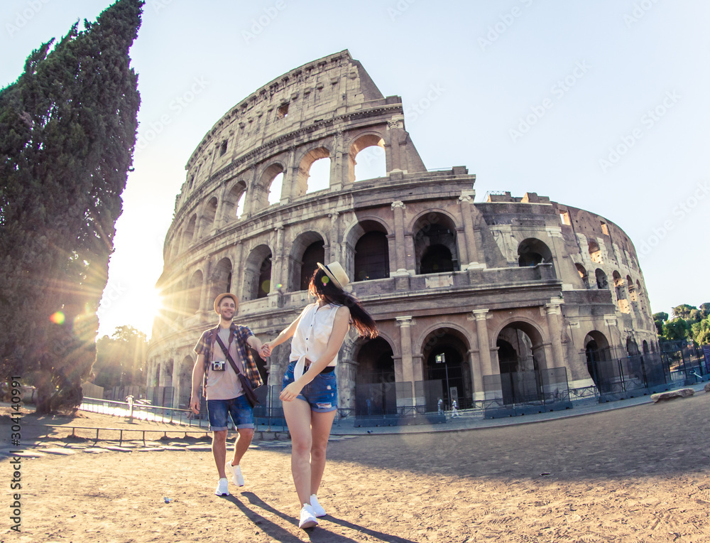 Young happy couple of tourist walking holding hands at Colosseum. Come with me. Rome, Italy - obrazy, fototapety, plakaty 