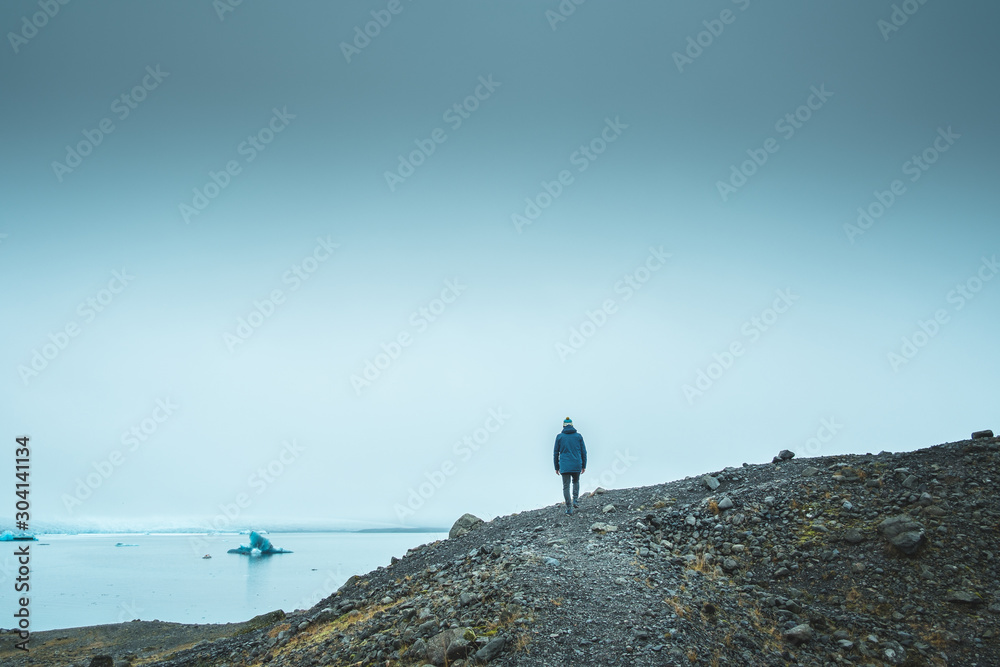 Jökulsárlón bay in Iceland. The man walk on the mountainous coast, in the background a hazy bay and icebergs floating in it.