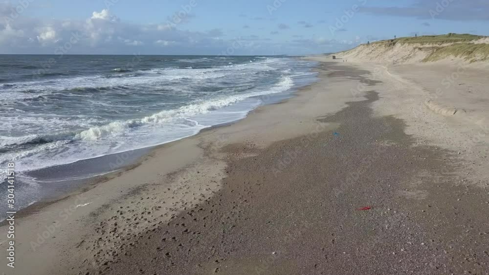 Ocean waves gently lap sandy beach with sand dunes, descending aerial Ocean waves gently lap sandy beach with sand dunes, descending aerial