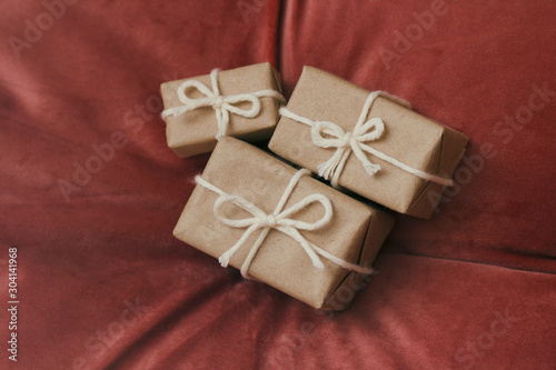 Presents for a Christmas. Gift boxes wrapped in craft paper and tie white string. Red velvet cloth background. Holiday mood. © exienator