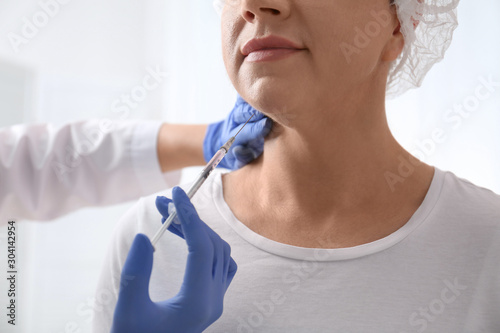 Mature woman with double chin receiving injection in clinic  closeup