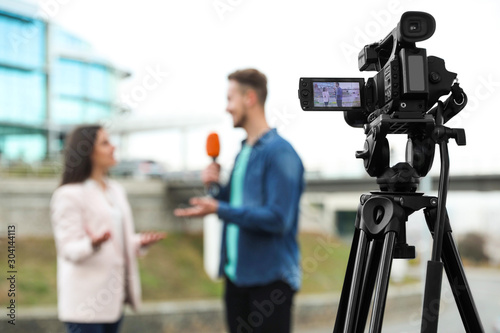 Fotografie Young journalist interviewing businesswoman on city street, focus on camera disp
