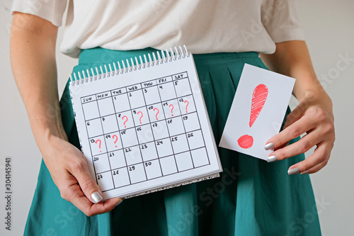 Woman holding calendar with marked missed period and exclmation mark. Unwanted pregnancy and delay in menstruation. photo
