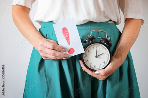 Woman holding clock at belly. Missed period, unwanted pregnancy and delay in menstruation.