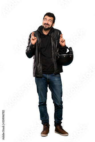 Full-length shot of Biker man with fingers crossing and wishing the best over isolated white background