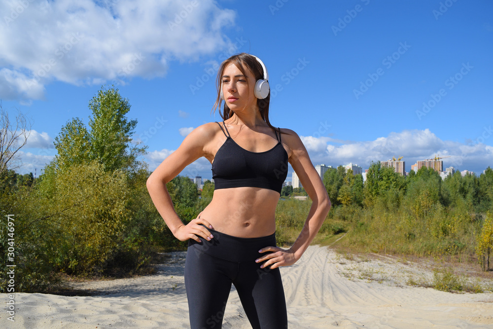 Sports girl in headphones stands on the background of nature in the country. Sports girl in headphones stands on the background of nature in the country.