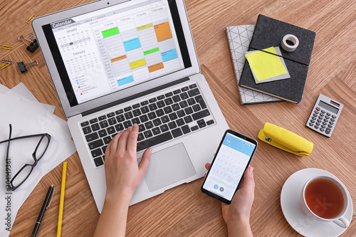 Woman using calendar on laptop and smartphone at wooden table, closeup