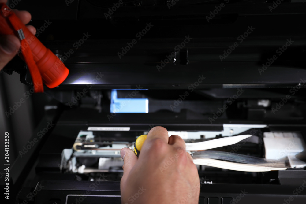 Repairman with flashlight fixing modern printer indoors, closeup