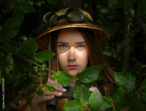 A young girl dresses up as an explorer. She wears a jungle hat and is seen in a forest environment.