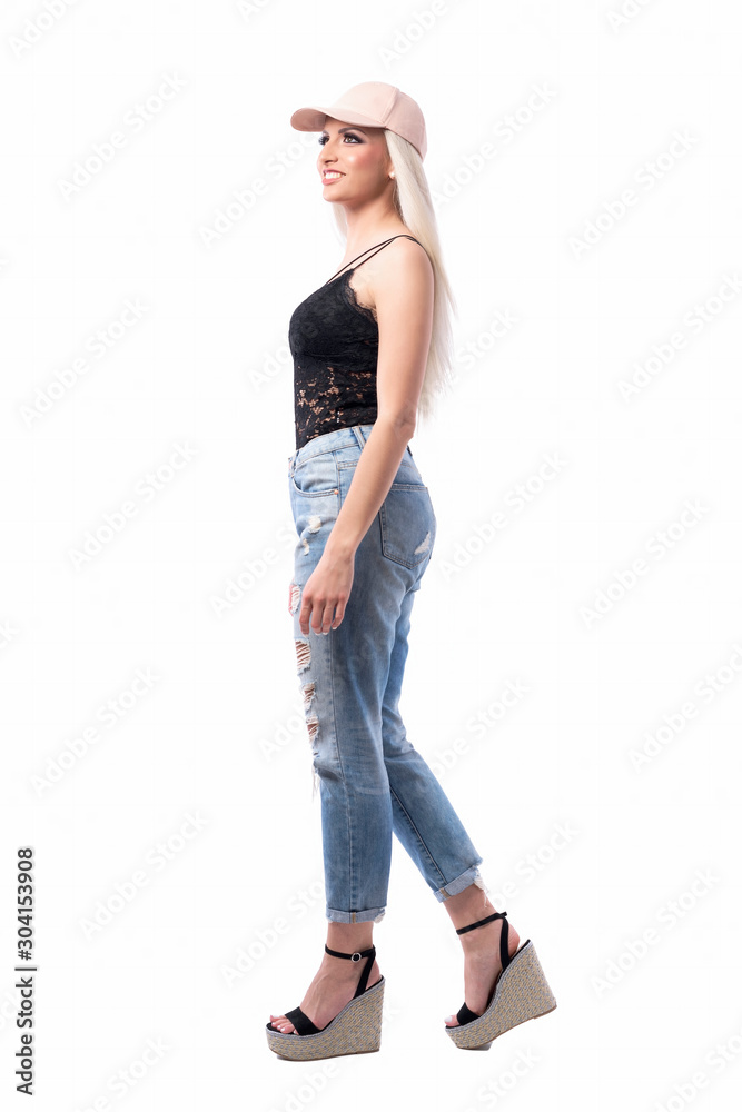 Side view of confident young urban happy blonde girl with baseball cap walking and looking up. Full body isolated on white background. Side view of confident young urban happy blonde girl with baseball cap walking and looking up. Full body isolated on white background.
