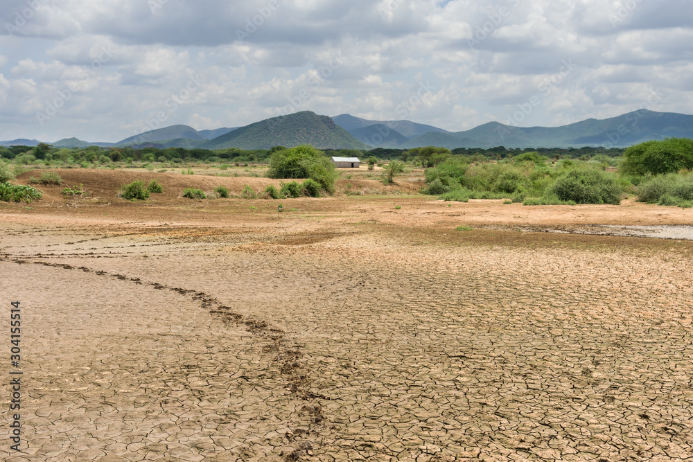 A dried up lake bed due to lack of rain with corrugated metal building and hills in background, Kajiado County, Kenya