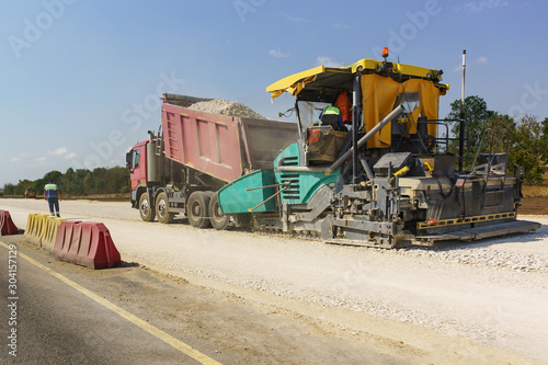 Construction of a new modern highway Tavrida in the Crimea. Backfilling of rubble from the truck into the capacity of the vibro-paver. Dusty Sunny day