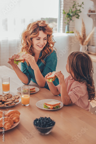 mother and daughter eating sandwiches for breakfast and looking at each other at the kitchen