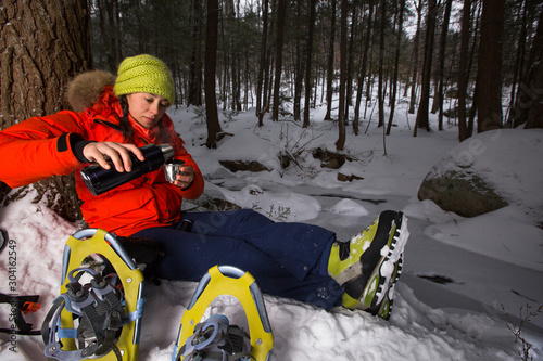 A woman admires the view of a frozen brook while taking a break from snowshoeing to have hot tea in the Green Hills Preserve near North Conway, New Hampsire. photo